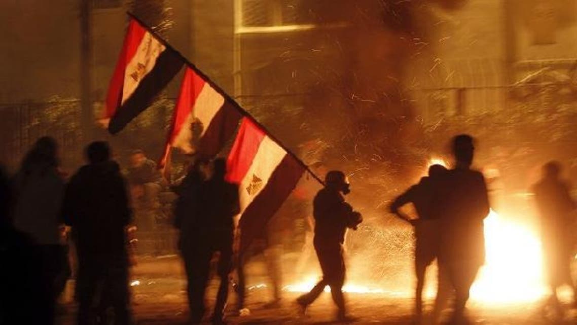 A protester opposing Egyptian President Mohamed Mursi carries national flags while walking near flames from Molotov cocktails thrown by protesters during clashes with riot police at the front road of Maspero, the Egyptian Radio & Television Union Headquarters, near Tahrir Square in Cairo January 25, 2013. (Reuters)