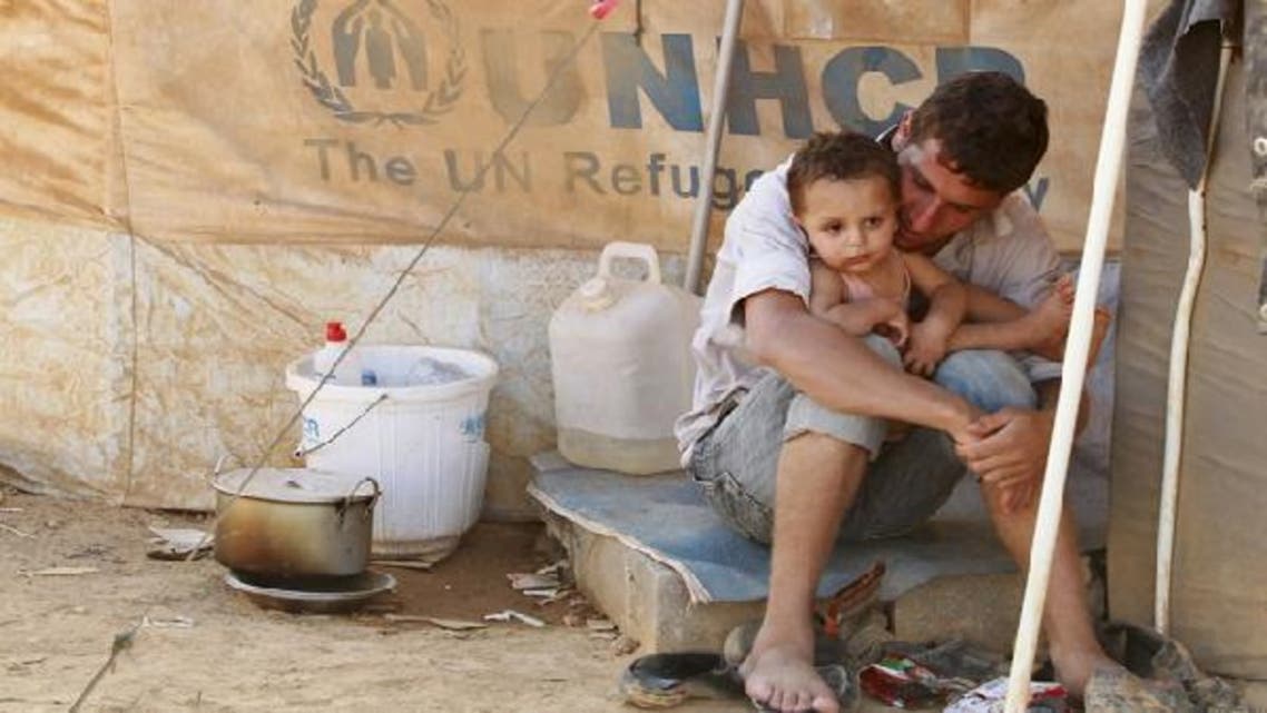 A Syrian refugee holds his child as he sits by his tent at al-Zaatri refugee camp in the Jordanian city of Mafraq, near the border with Syria. (Reuters)