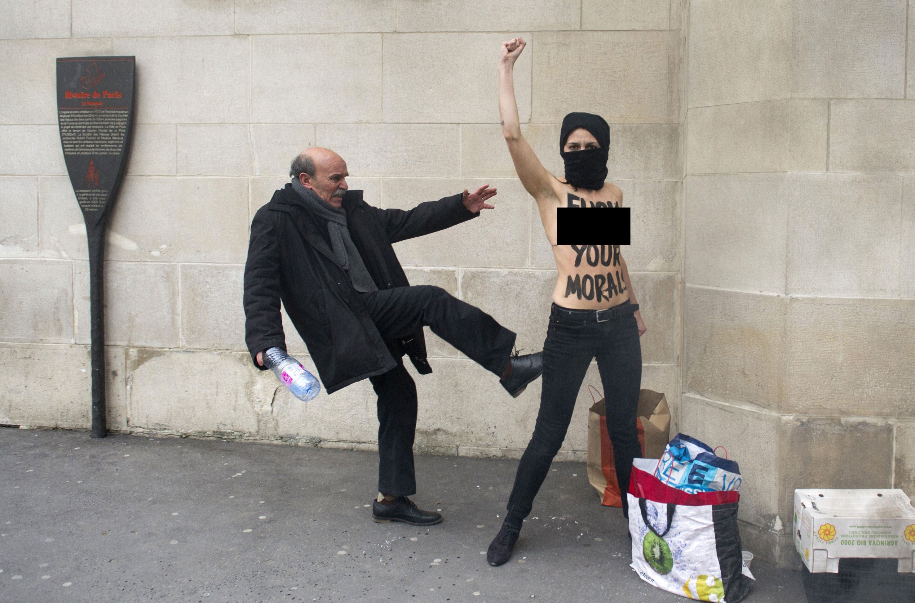 A man kicks a topless activist of the Ukrainian feminist movement Femen as she raises her fist to protest against Islamists in front of the Great Mosque of Paris on April 3, 2013 in Paris. (AFP)