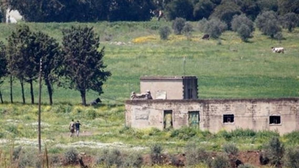 Syrian soldiers walk in a field in the Syrian village of Al Arida Al Gharbia as seen from the northern Lebanese village of Wadi Khaled near the Lebanese-Syrian border