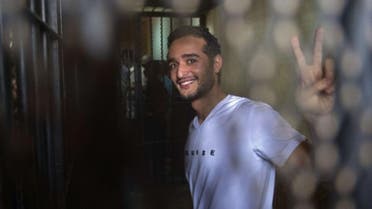 Egyptian political activist Ahmed Douma smiles and flashes the "V" for victory sign as he stands behind dock bars during his trial in Cairo on 13 May 2013. (AFP)