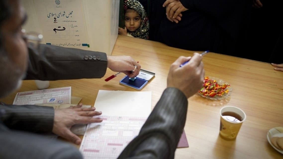 A girl stands next to a ballot box as election officials register a voter at a polling station at the Massoumeh shrine in Qom on March 2, 2012. (AFP)