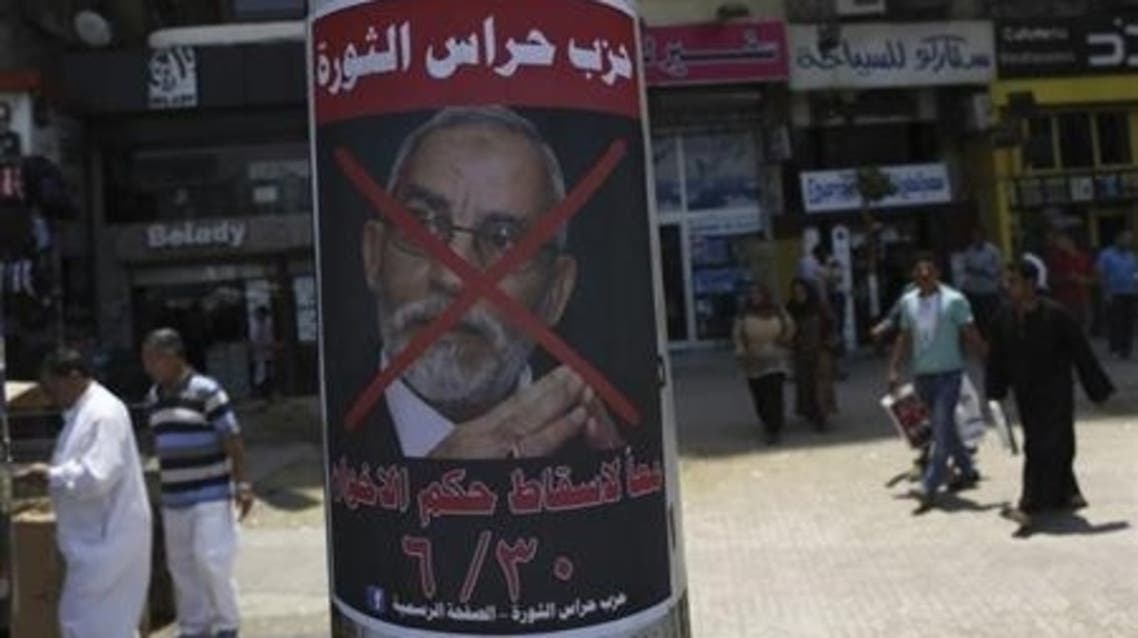 People walk past a defaced poster of Muslim Brotherhood leader Mohammad Badie with Arabic text which reads “Together to down brotherhood’s power” near Tahrir Square in Cairo June 23, 2013. (File Photo: reuters)