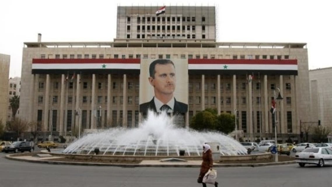 A woman walks past the central bank building decorated with a banner of Bashar al-Assad in Damascus on February 28, 2012. (File Photo:AFP)