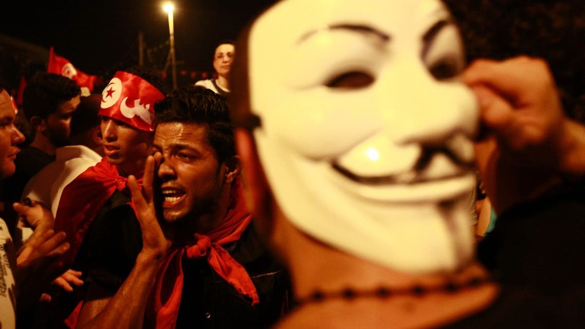An anti-government protester wears a Guy Fawkes mask as another shouts slogans during a demonstration in Tunis August 6, 2013.