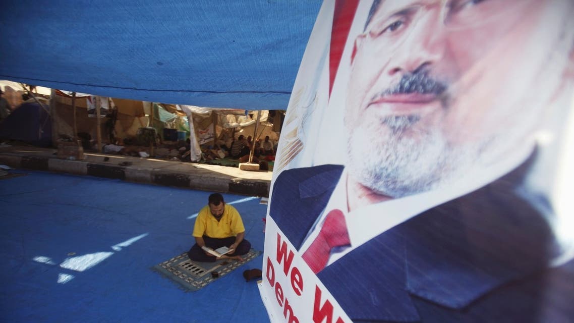 A poster of deposed Egyptian President Mohamed Mursi is seen, as a member of the Muslim Brotherhood and supporter of Mursi reads the Koran in his tent at Rabaa Adawiya Square