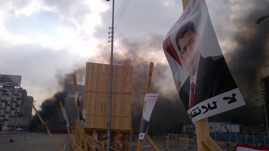 A poster of deposed Islamist President Mohamed Mursi is pictured in front of rising smoke during clashes between riot police and members and supporters of the Muslim Brotherhood, at Rabba el Adwia Square in Cairo August 14, 2013.