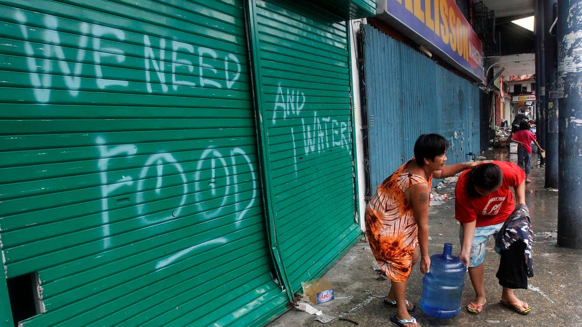 Residents carry a plastic container of drinking water as they walk past a graffiti calling for help after Typhoon Haiyan devastated Tacloban city, central Philippines. (Reuters)