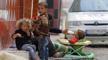 Children eat as a baby drinks milk along a street in the Duma neighborhood of Damascus Nov.12, 2013. (Reuters)