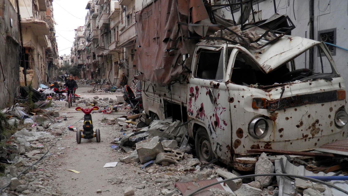 A girl rides a bicycle amidst damaged buildings and vehicles along a street in the besieged area of Homs reuters