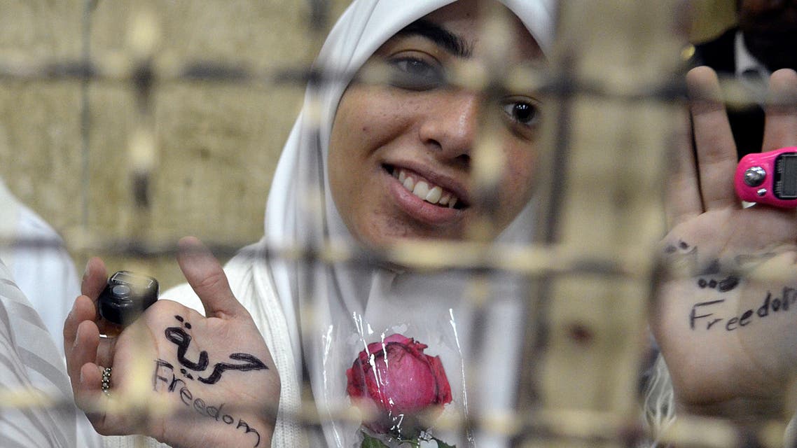 Egyptian women members of the Muslim Brotherhood hold roses as they stand in the defendants' cage dressed in prison issue white during their trial in at the court in Alexandria on Dec.7, 2013. (AFP)