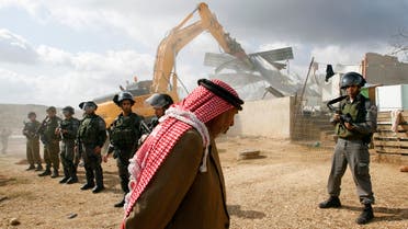 A Palestinian man walks past Israeli border police standing guard as a bulldozer demolishes a structure in the West Bank village of Beit Hanina, near Jerusalem Nov. 24, 2011. (Reuters)