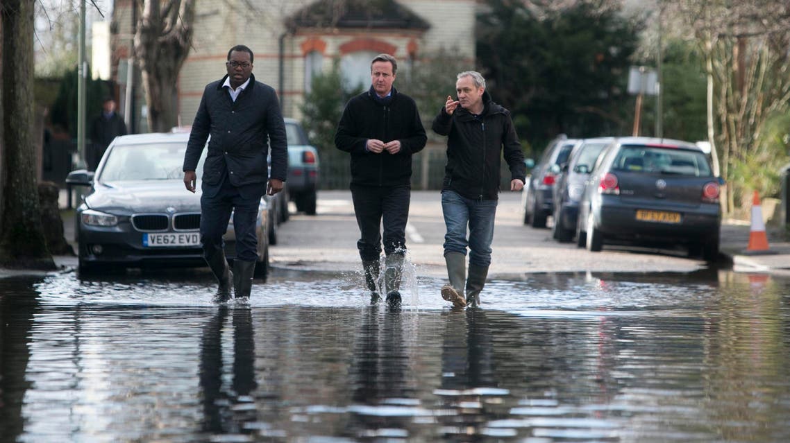 Britain's Prime Minister David Cameron (C) speaks with resident Ray Connerlley (R) and Kwasi Kwarteng, the MP for Spelthorne, as they walk through flood water in Guildford Street in Staines-upon-Thames, southwest of London February 11, 2014. reut