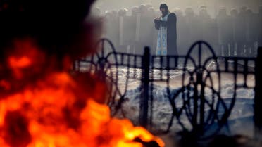 A priest prays in front of riot police during clashes with anti-government protesters in Kiev January 25, 2014. reuters