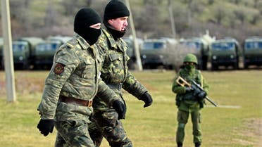 Ukrainian servicemen walk past an armed man, believed to be Russian, at the Ukrainian military base in Perevalnoye, outside Simferopol March 17, 2014. (Reuters)