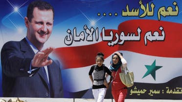 Young Syrian women walk past a huge billboard bearing a portrait of Syrian President Bashar al-Assad, with the slogan "Yes for Assad... Yes for a secure Syria" afp