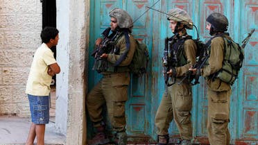 A Palestinian boy stands next to Israeli soldiers as they take part in operation to locate three Israeli teens near the West Bank City of Hebron Reuters