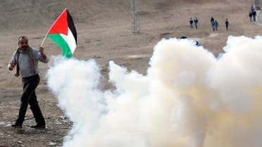 A Palestinian protester holds a Palestinian flag as he walks next to tear gas fired by Israeli soldiers during clashes following a protest near the West Bank city of Jericho November 28, 2014. (Reuters)