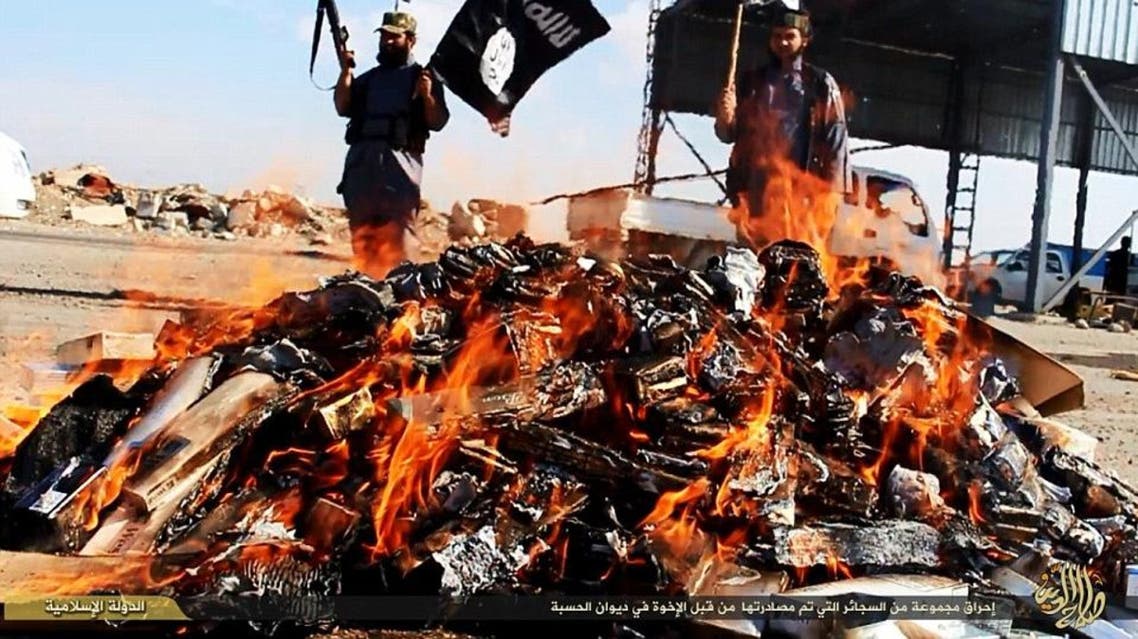 A pile of cigarettes, banned in ISIS-held areas, burn as the militants watch over. (Photo courtesy: YouTube)