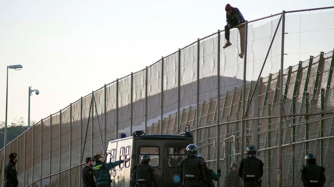 n African migrant sits atop a border fence, above Spanish Civil Guard officers, during an attempt to cross into Spanish territories, between Morocco and Spain's north African enclave of Melilla December 19, 2014. REUTERS