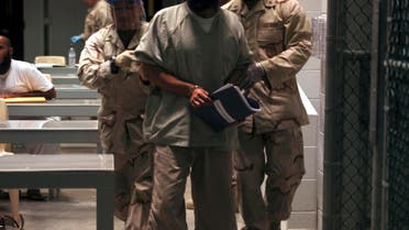 A Guantanamo detainee carries a workbook while escorted by guards who wear rubber gloves and face masks after attending a Life Skills class in the Camp 6 high-security detention facility on Guantanamo Bay U.S. Naval Base in Cuba. (File photo: AP)