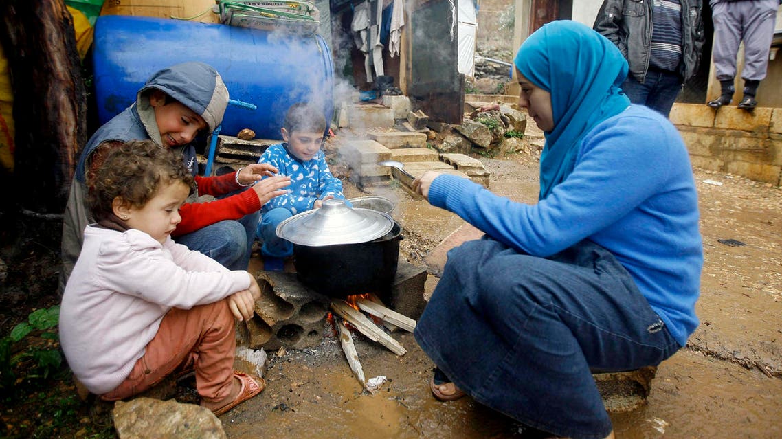 a Syrian refugee woman with her children prepares food near her tent as a heavy snowstorm batters the region. (AP)