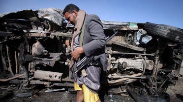 A Houthi militant stands next to a destroyed vehicle, which belongs to a Houthi man, after an improvised explosive device under it detonated in Sanaa January 25, 2015. reuters