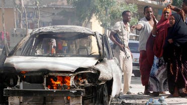 A security officer and residents stand near the wreckage of a car that exploded from a bomb planted in it, killing one person and injuring two others, in Somalia's capital Mogadishu, Feb.27, 2015. (File Photo: Reuters)