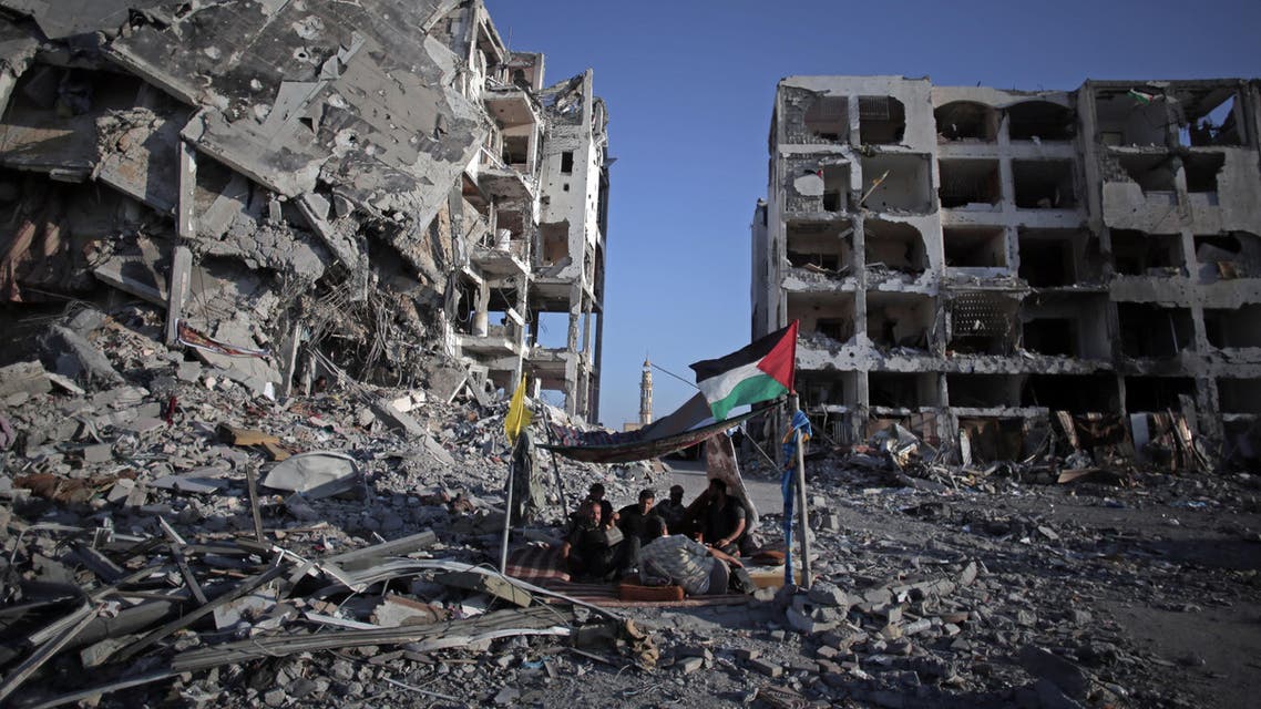 In this Aug. 11, 2014 file photo, Palestinian Ziad Rizk, 38, sits with others in a shelter made of a blanket stretched over four boles next to one of the destroyed Nada Towers, where he lost his apartment and clothes shop. (AP)