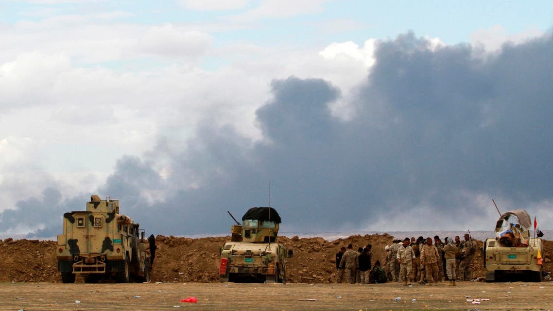 Iraqi soldiers gather near their vehicles as smoke rises from oil wells in the Ajil field east of the city of Tikrit in the Salahuddin province, March 4, 2015. (Reuters)