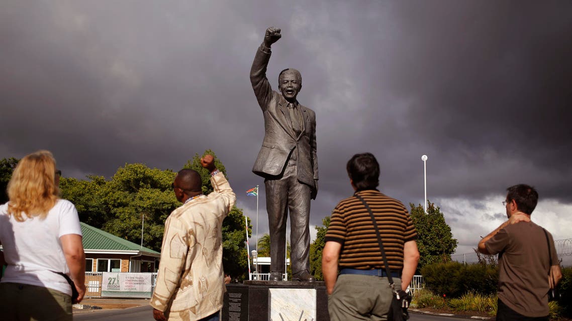 A tour guide, second left, speaks to French tourists as he, mimics the statue of former South African President Nelson Mandela with a raised fist outside the former Victor Verster prison, renamed to Drakenstein Correctional center near the town of Franschhoek, South Africa, Tuesday, Feb. 10, 2015. (AP)