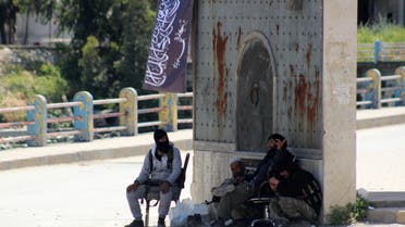 Armed fighters loyal to Al-Qaeda's Syrian affiliate, Al-Nusra Front, sit under a gate at the entrance of the northern town of Jisr al-Shughur on April 26, 2015.  AFP 
