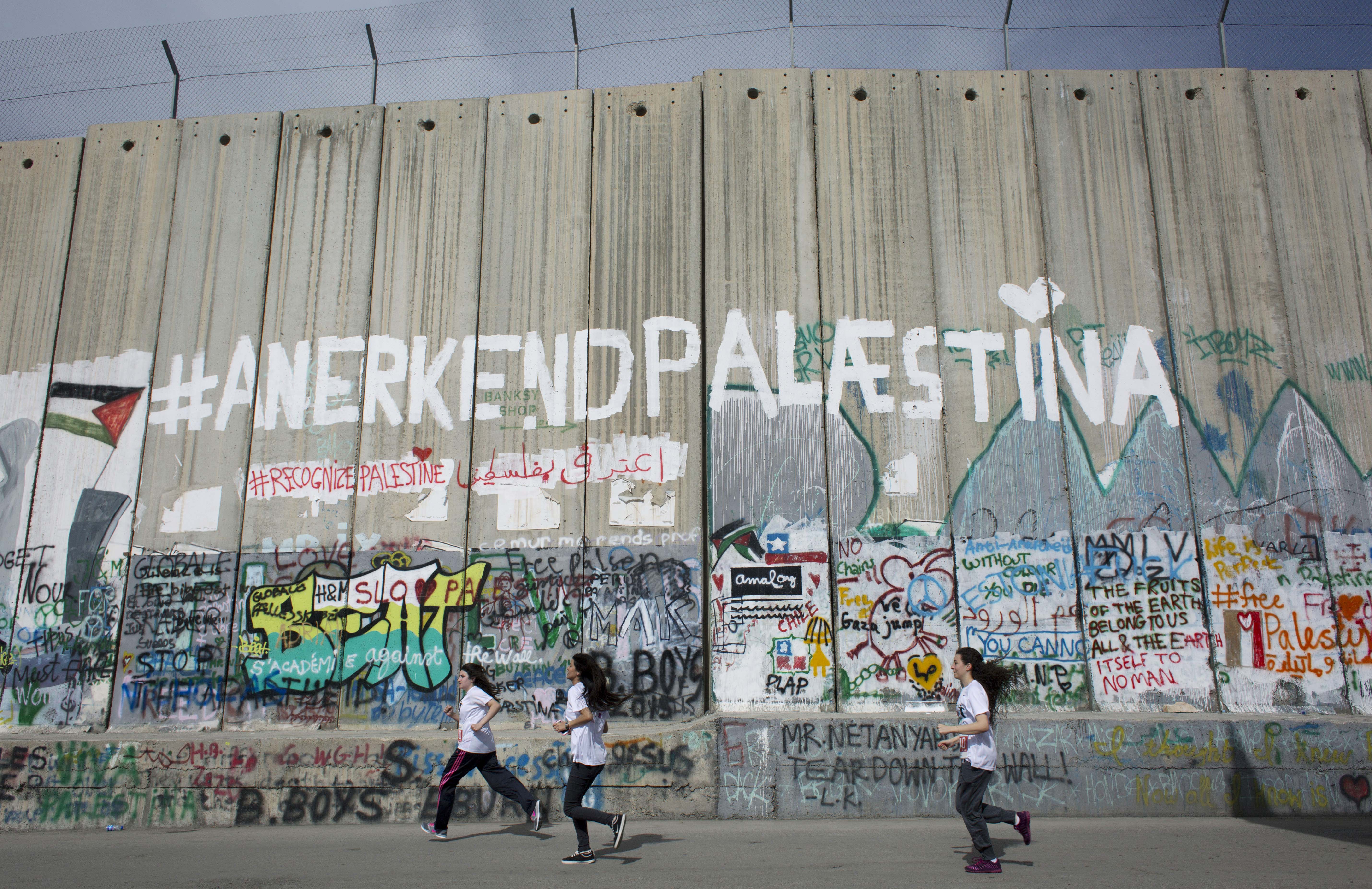 Runners taking part in the Palestine Marathon pass by the Israeli separation barrier in the West Bank city of Bethlehem, Friday, March 27, 2015. (AP)
