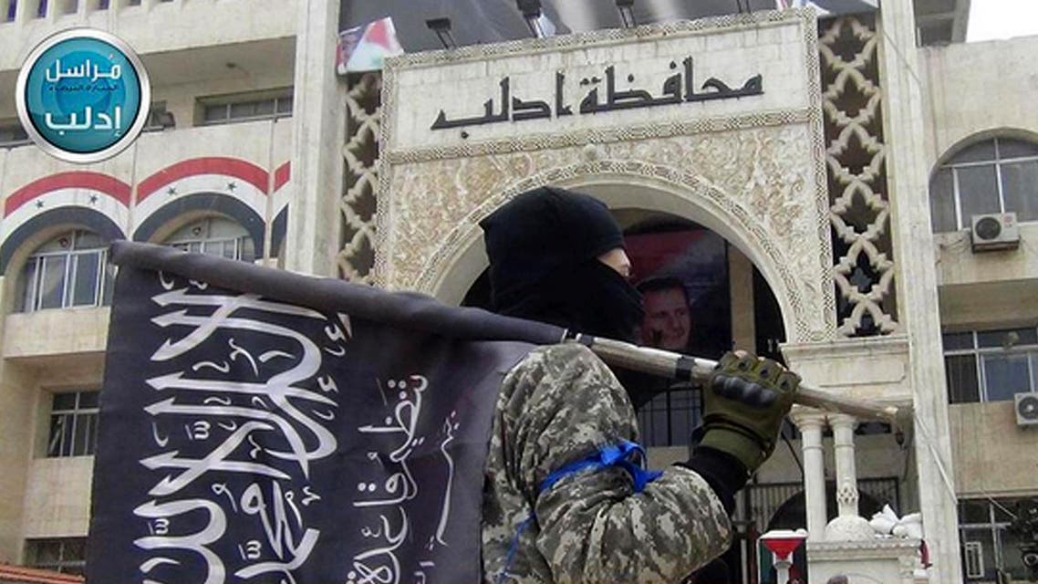 a fighter from Syria's al-Qaida-linked Nusra Front holds his group flag as he stands in front of the governor building in Idlib province, north Syria. AP