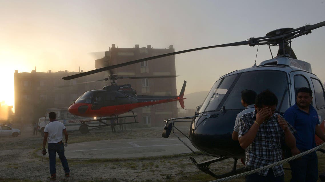 PRA1202 - Kathmandu, -, NEPAL : Nepalese bystanders shield themselves from dust as a helicopter bearing the bodies of helicopter crash victims, lands upon arrival at Teaching hospital in Kathmandu on June 2, 2015. Nepalese troops recovered four bodies after a helicopter which had been delivering relief supplies crashed in a region devastated by twin earthquakes in recent weeks, the army and police said. The aircraft from Kathmandu-based Mountain Helicopters came down in a forested area north of the capital, police said. AFP PHOTO / Prakash MATHEMA