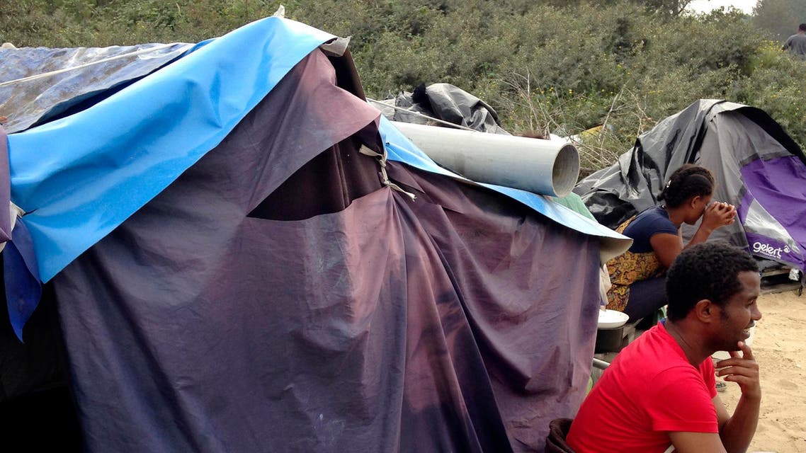 In this photo taken Sunday, Sept. 7, 2014, migrants sit by a tent at a makeshift camp in Calais, northern France. Migrants huddle in shanty-towns in Calais, gazing out at a tantalizingly narrow stretch of water toward Britain - the land they see as their Eldorado. They are pouring into the French port city at an ever-faster pace, overwhelming police with aggressive new tactics in their bid to cross the English Channel. (AP Photo/Elaine Ganley)