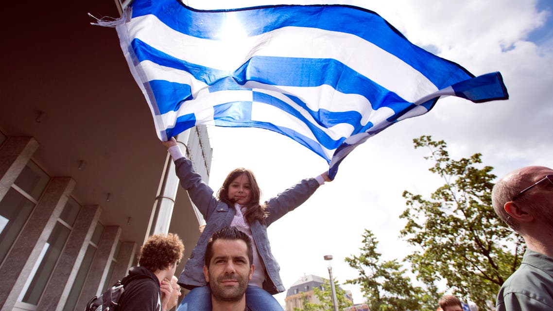 A girl sits on her father's shoulders as she unfurls the Greek flag during a protest march in solidarity with Greece in the center of Brussels on Sunday, June 21, 2015. (AP)