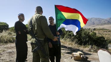 A member of the Druze community holds a Druze flag as he speaks to an Israeli soldier near the border fence between Syria and the Israeli-occupied Golan Heights, near Majdal Shams. (File: Reuters)