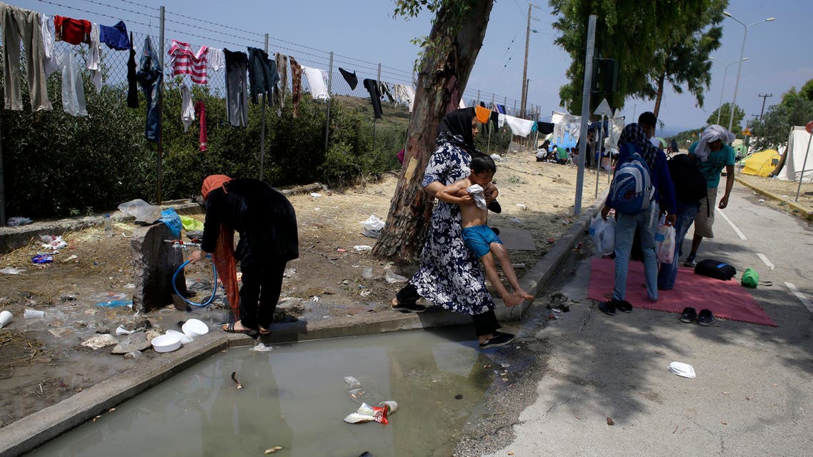 In this photo taken on Tuesday, June 16, 2015 a woman holds up a child to pass dirty water at a migrant and refugee camp in Mytilene, on the northeastern Greek island of Lesbos (AP)