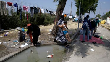In this photo taken on Tuesday, June 16, 2015 a woman holds up a child to pass dirty water at a migrant and refugee camp in Mytilene, on the northeastern Greek island of Lesbos (AP)