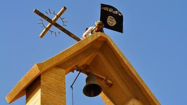 In this photo released on March 7, 2015 by a militant website, which has been verified and is consistent with other AP reporting, a member of the Islamic State group holds the IS flag as he dismantles a cross on the top of a church in Mosul, Iraq.
