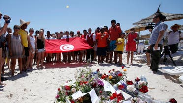 People, some displaying a Tunisian flag, stand in silence next to flowers during a gathering at the scene of the attack in Sousse, Tunisia, Sunday, June 28, 2015. AP 