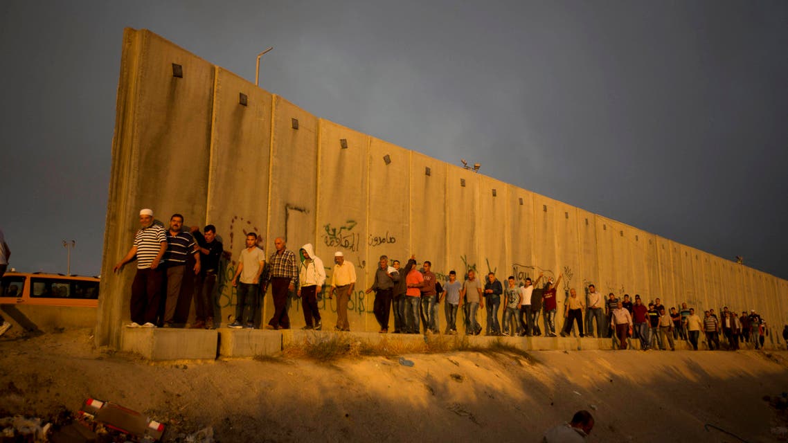 Palestinian men walk past a section of Israel's separation barrier to cross the Qalandia checkpoint on their way to pray at the Al-Aqsa Mosque in Jerusalem. (AP)
