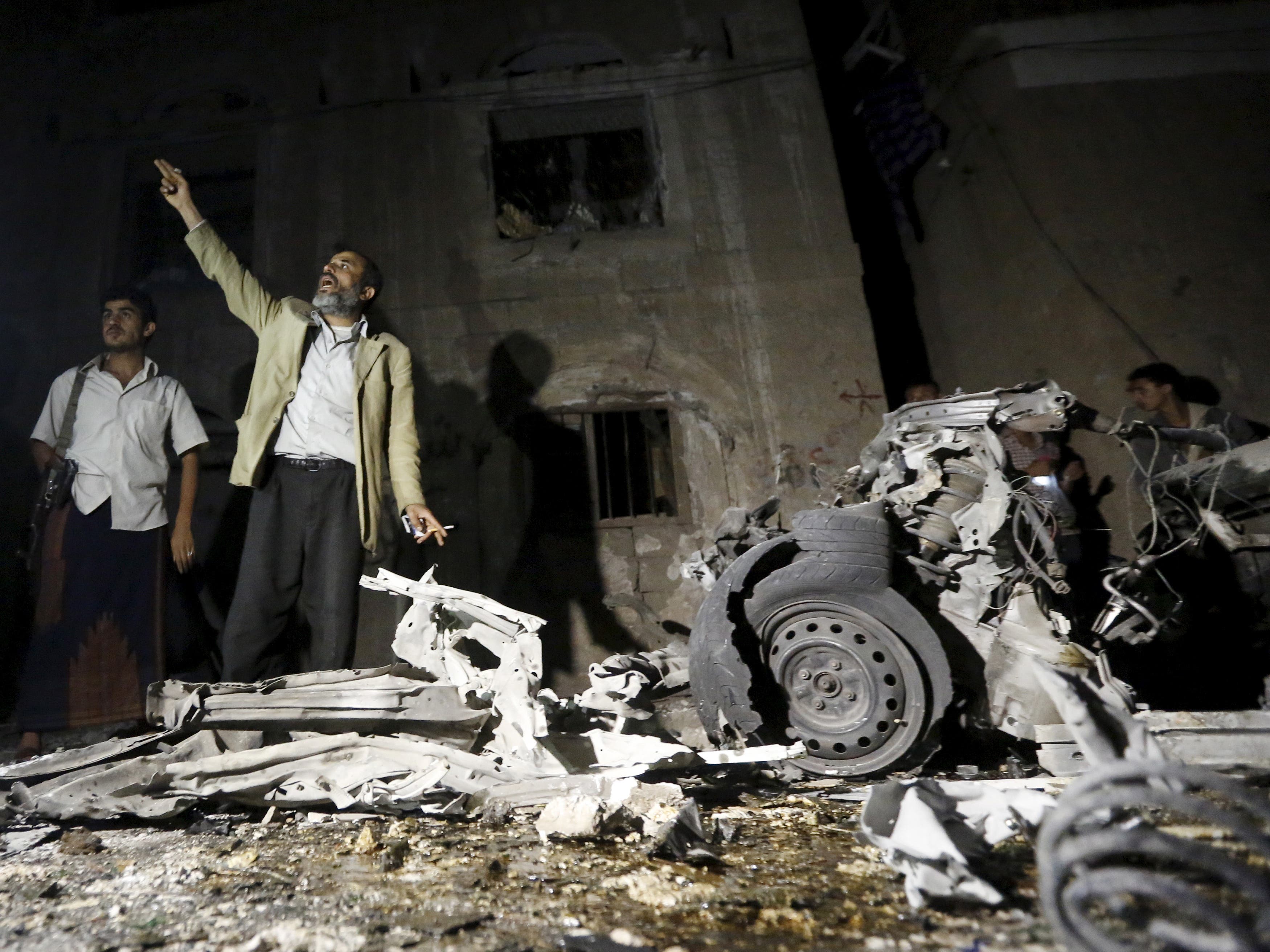 People stand next to a damaged house at the site of a car bomb attack in Yemen's capital Sanaa June 29, 2015. 