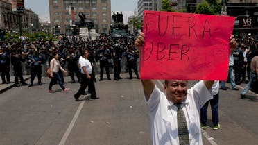 A man holds a sign that reads in Spanish "Uber Out" in front of a line of riot police as thousands of taxi drivers blocked the main streets to protests against Uber in Mexico City. (File Photo: AP)