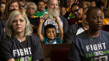 David Lazo, 5, center, with his father Francisco, right, raises a dollar bill as workers await the Los Angeles City Council's vote to raise the minimum wage in the city to $15 an hour by 2020 in Los Angeles Wednesday, June 3, 2015. 