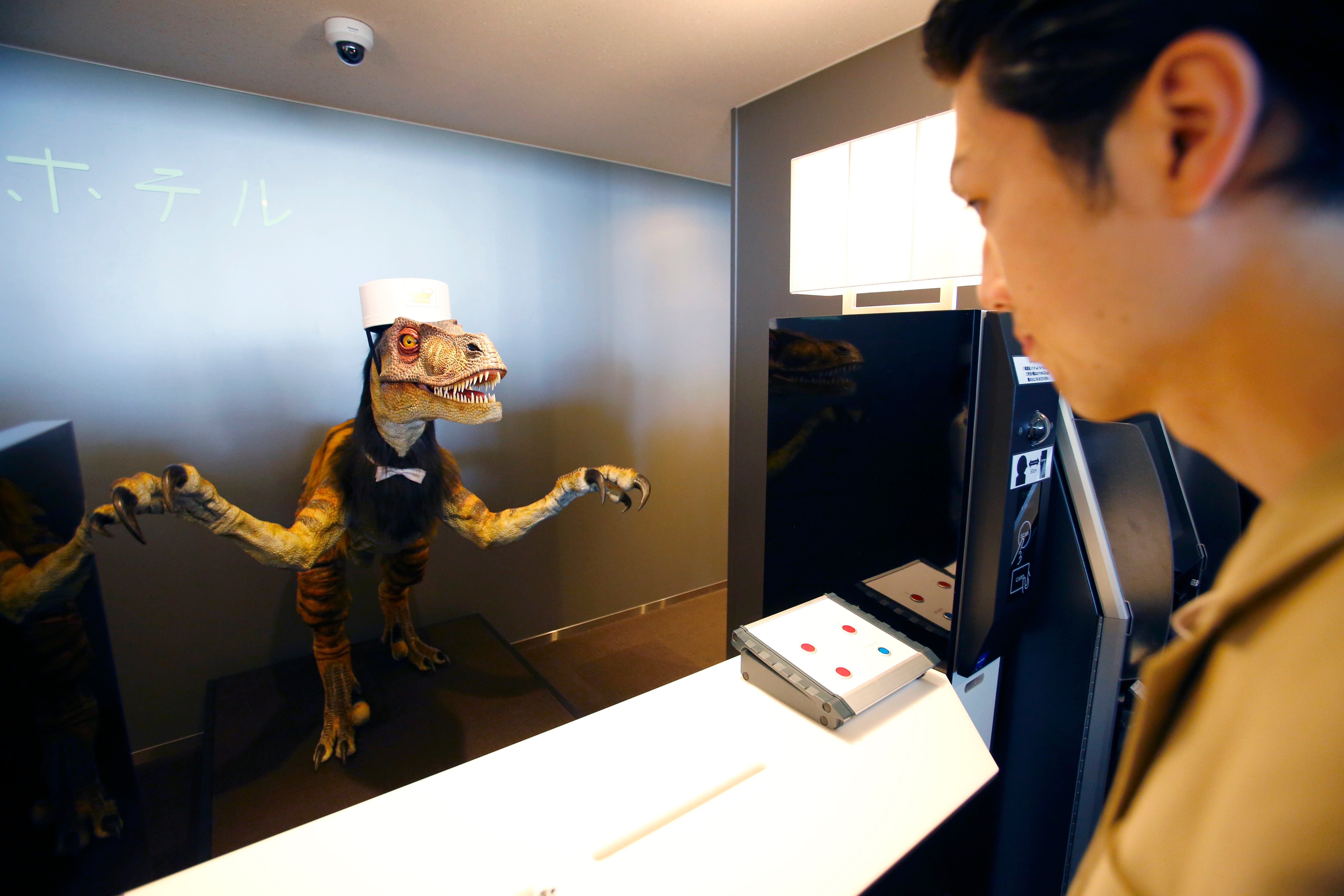 A receptionist dinosaur robot greets a hotel employee demonstrating how to check in for the media at the new hotel, aptly called Henn na Hotel or Weird Hotel, in Sasebo, southwestern Japan, Wednesday, July 15, 2015. 
