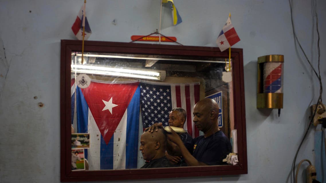 Eugenio Lafargue is reflected in a mirror as he cuts a client's hair inside his barbershop decorated with a Cuban and U.S. flag in Havana, Cuba, Saturday, July 18, 2015. Washington and Havana plan to officially restore diplomatic relations on Monday with the reopening of their embassies. (AP Photo/Ramon Espinosa)