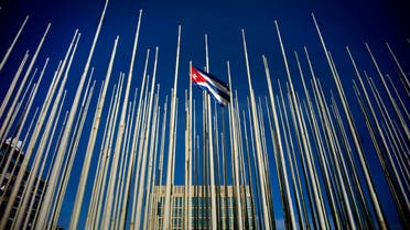 A Cuban flag flies among empty flag polls near the U.S. Interests Section building, behind, in Havana, Sunday, July 19, 2015. 