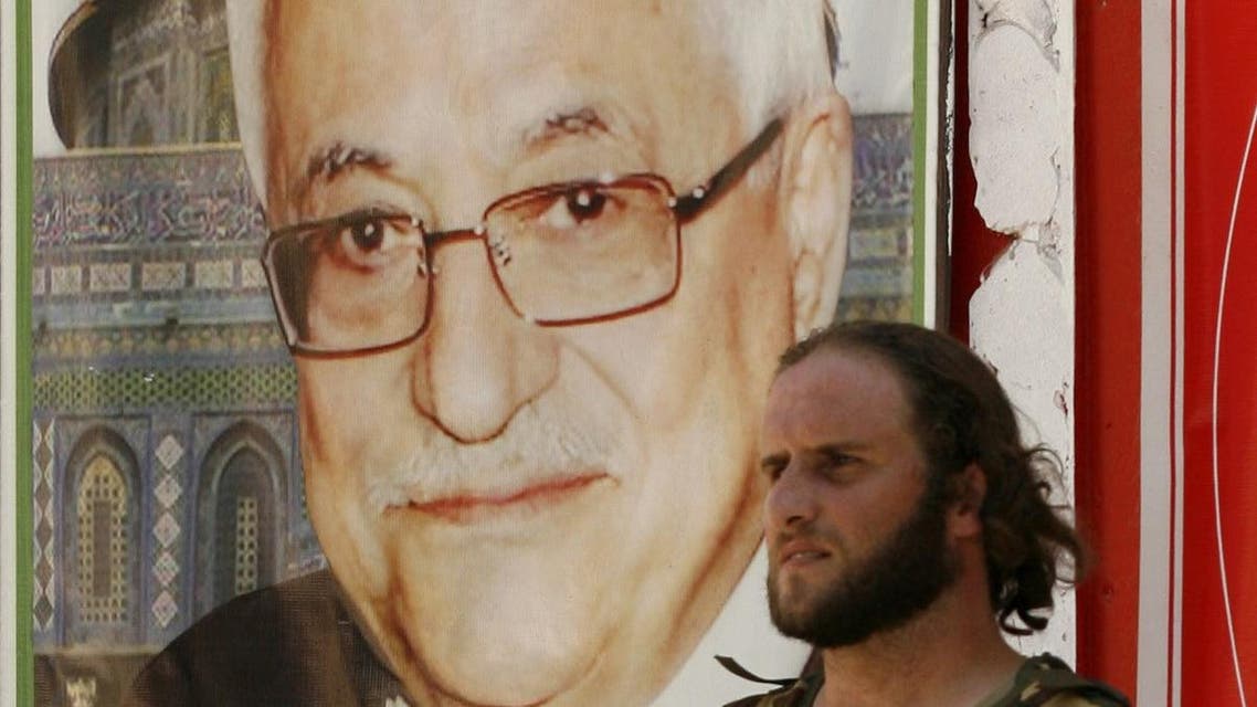 MZ01 - Ain El-Helweh, -, LEBANON : An armed man stands next to a poster bearing the portrait of Palestinian president Mahmud Abbas on July 25, 2015, in Lebanon's southern Palestinian refugee camp of Ain El-Helweh, after Talal al-Ourdouni, a senior member of Abbas' Fatah movement, was shot dead in the camp. AFP PHOTO / MAHMOUD ZAYYAT